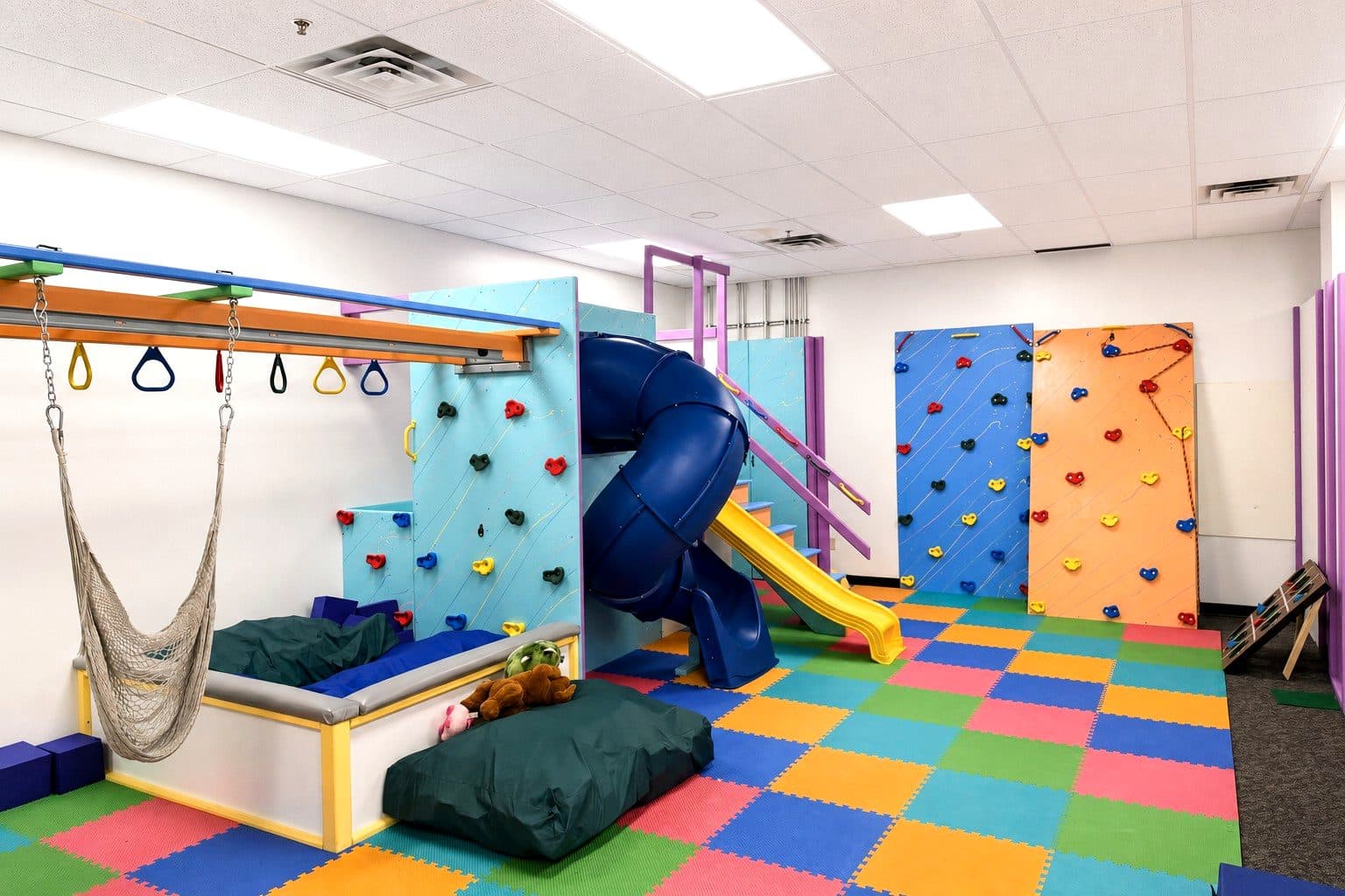 The sensory gym at our Eagan clinic, with a slide, swings, and a climbing wall over a padded floor